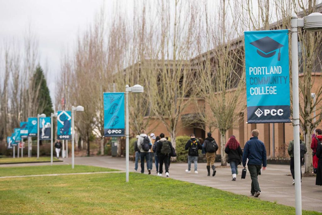 Students walk along a sidewalk past banners that read Portland Community College