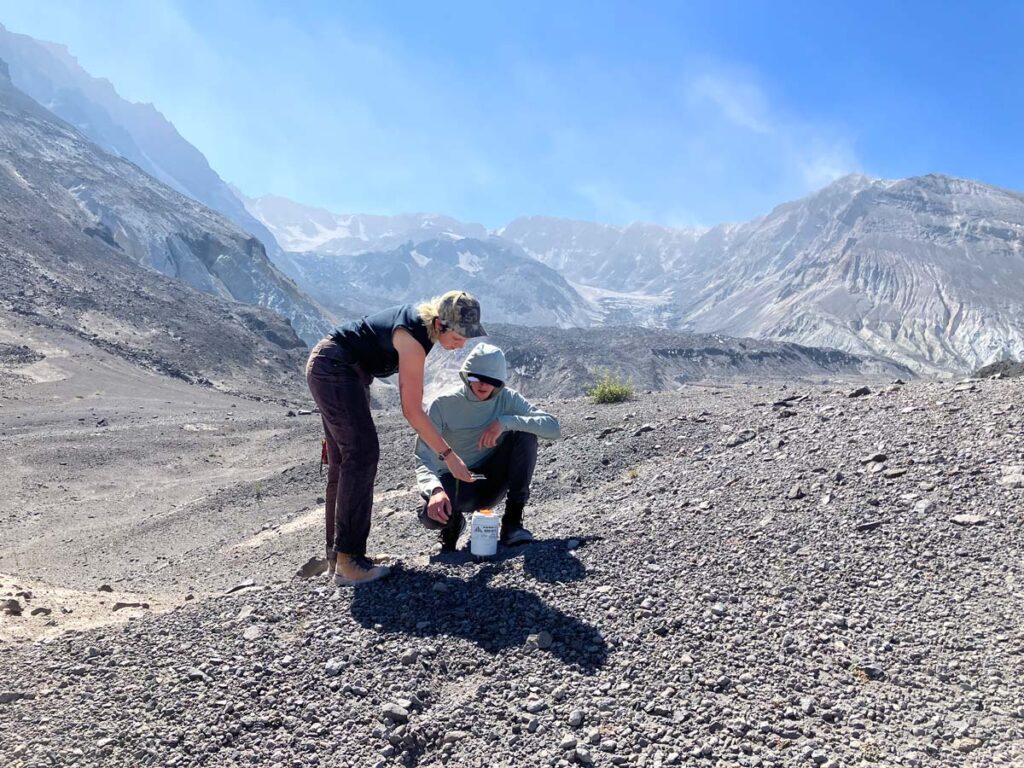 Two members of the Cascadia Region Earthquake Science Center take readings from equipment in a remote mountainou s area.