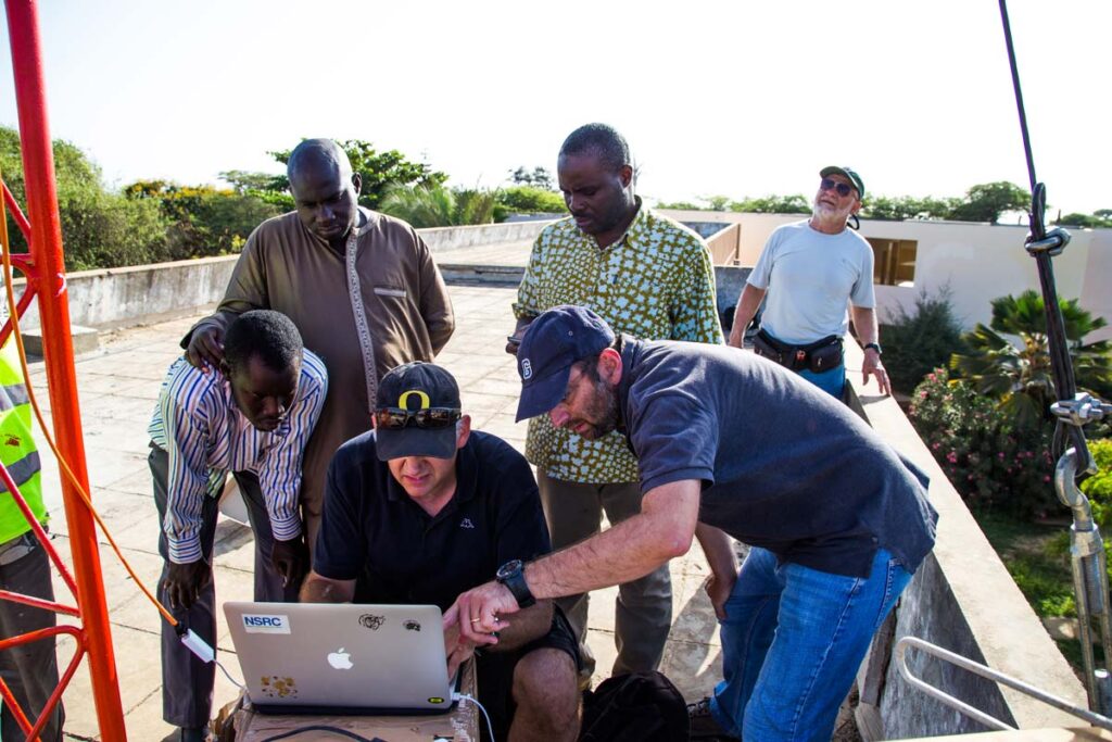 NSRC staff and community members huddle around a laptop on the roof of a building.